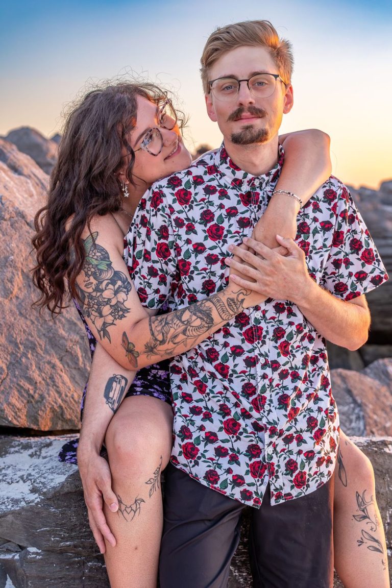 Couple in matching floral shirts posing on rocky beach during golden hour