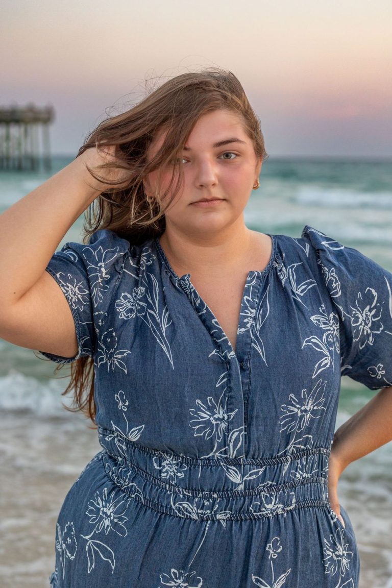 Portrait series in blue floral dress with beach and pier in background during sunset