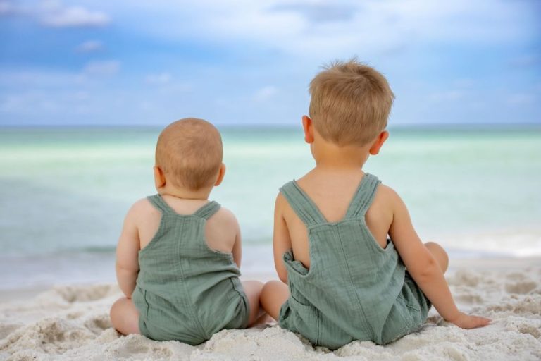 Two children in matching green outfits sitting together on a sandy beach
